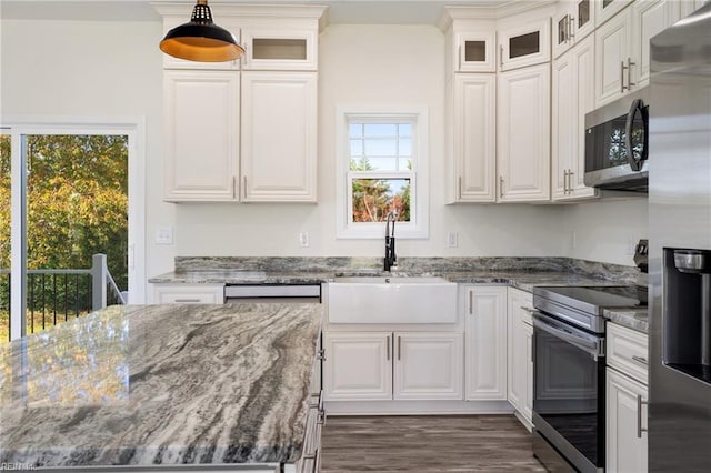 kitchen with white cabinetry, sink, hanging light fixtures, dark stone counters, and appliances with stainless steel finishes