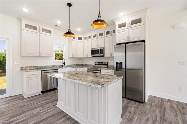 kitchen featuring light stone counters, stainless steel appliances, a kitchen island, white cabinetry, and hanging light fixtures