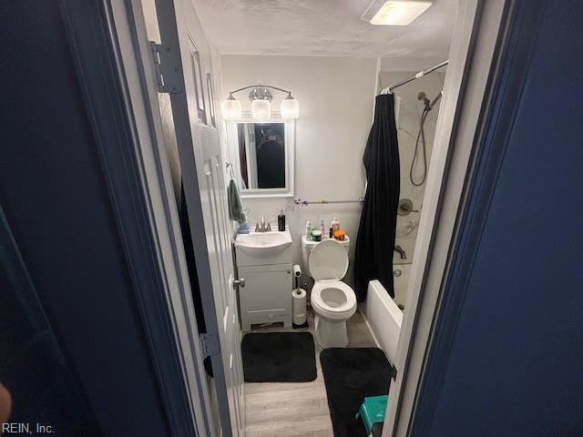 full bathroom featuring hardwood / wood-style flooring, vanity, shower / bath combination with curtain, and toilet