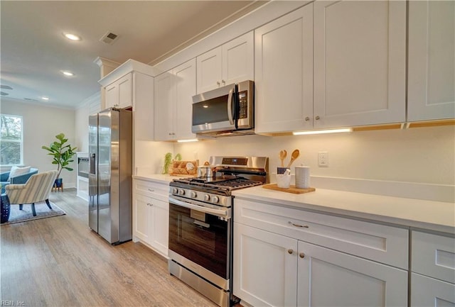 kitchen with white cabinets, appliances with stainless steel finishes, light hardwood / wood-style flooring, and ornamental molding