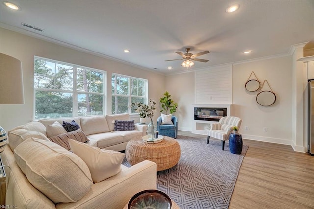 living room featuring crown molding, a fireplace, ceiling fan, and hardwood / wood-style flooring