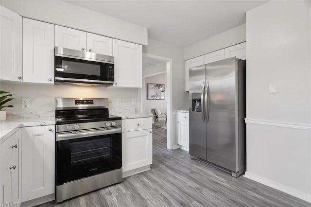 kitchen featuring light stone counters, white cabinets, stainless steel appliances, and light wood-type flooring