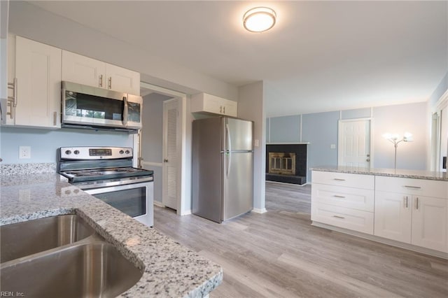 kitchen featuring light stone counters, white cabinets, light wood-type flooring, and appliances with stainless steel finishes