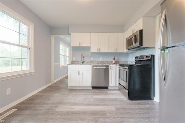 kitchen with appliances with stainless steel finishes, light wood-type flooring, light stone counters, sink, and white cabinets