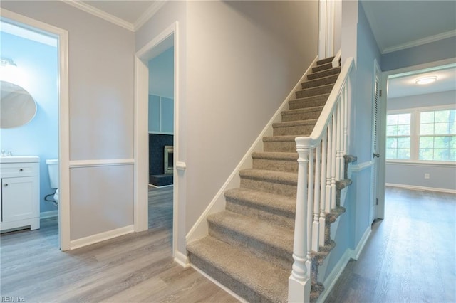 staircase featuring a brick fireplace, wood-type flooring, and ornamental molding