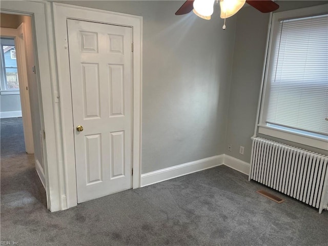 empty room with dark colored carpet, radiator, and ceiling fan