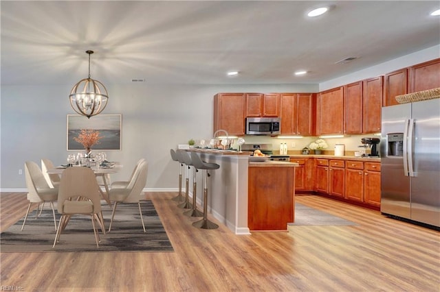 kitchen with a chandelier, stainless steel appliances, decorative light fixtures, and light hardwood / wood-style floors