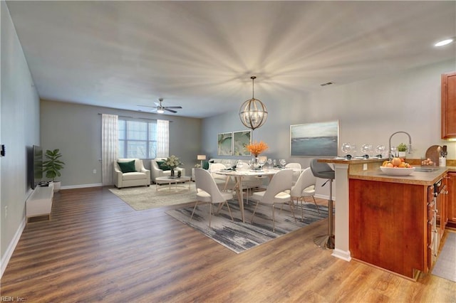 dining area featuring ceiling fan with notable chandelier, light hardwood / wood-style floors, and sink