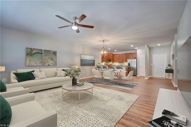 living room featuring ceiling fan with notable chandelier and light hardwood / wood-style floors