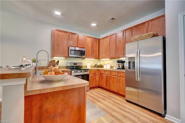 kitchen with sink, kitchen peninsula, stainless steel appliances, and light hardwood / wood-style flooring