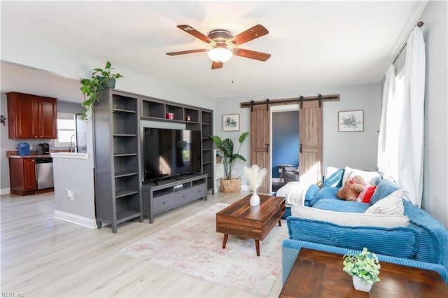 living room with a barn door, ceiling fan, and light wood-type flooring