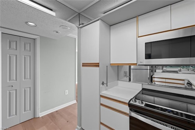 kitchen featuring a textured ceiling, stainless steel appliances, white cabinetry, and light hardwood / wood-style flooring