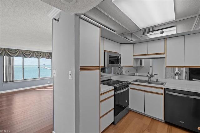 kitchen with stainless steel appliances, sink, a water view, light hardwood / wood-style floors, and white cabinetry