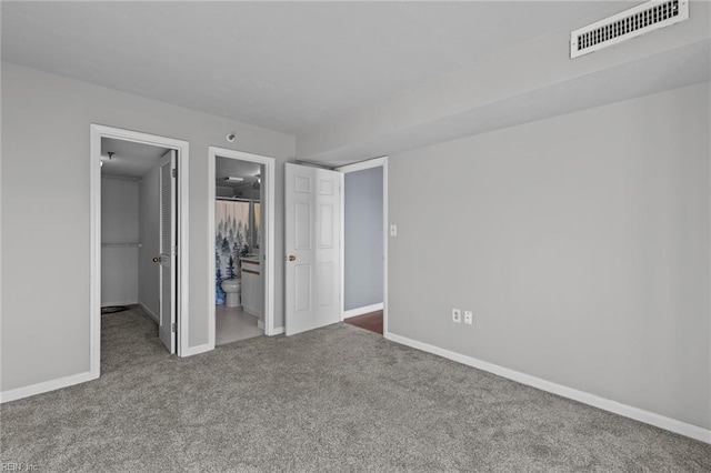 unfurnished bedroom with a walk in closet, carpet floors, a closet, and connected bathroom