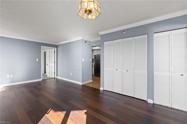 unfurnished bedroom featuring black refrigerator, dark hardwood / wood-style flooring, crown molding, and multiple closets