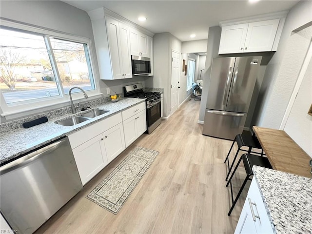 kitchen featuring white cabinets, sink, light wood-type flooring, light stone countertops, and appliances with stainless steel finishes