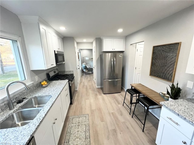 kitchen with white cabinets, stainless steel appliances, light stone countertops, and sink