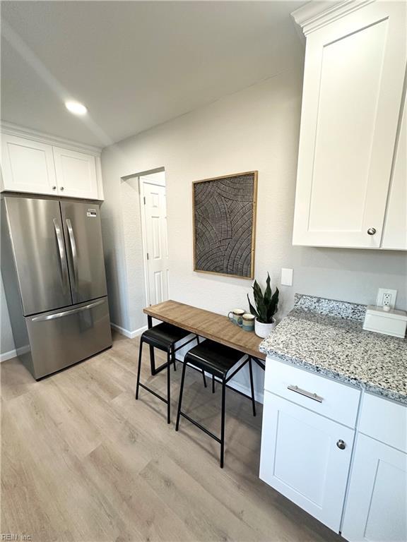 kitchen with stainless steel refrigerator, light stone counters, white cabinets, and light hardwood / wood-style floors