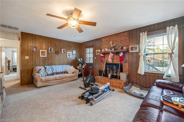 carpeted living room featuring a fireplace, ceiling fan, and wooden walls