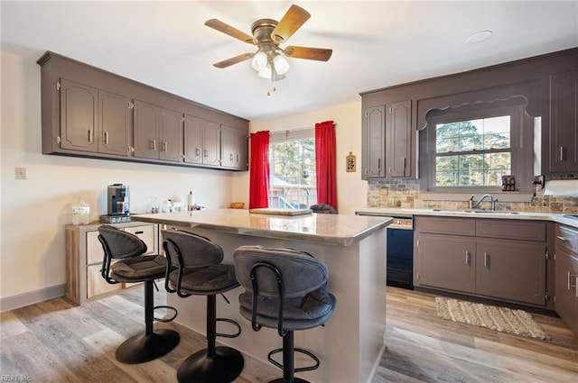 kitchen featuring sink, light wood-type flooring, black dishwasher, a kitchen bar, and kitchen peninsula