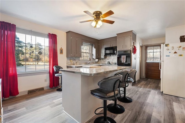 kitchen with black appliances, light hardwood / wood-style flooring, ceiling fan, tasteful backsplash, and a breakfast bar area