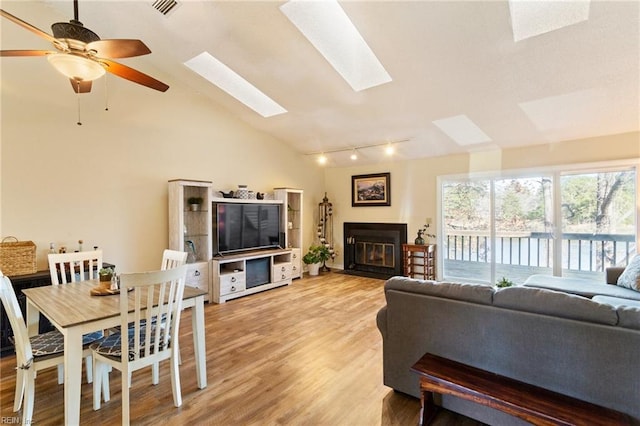 living room featuring light wood-type flooring, rail lighting, ceiling fan, and vaulted ceiling with skylight