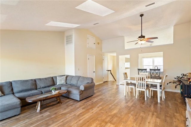 living room featuring light hardwood / wood-style flooring, ceiling fan, and vaulted ceiling with skylight