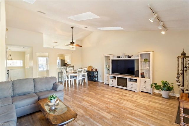 living room with ceiling fan, vaulted ceiling with skylight, light hardwood / wood-style floors, and track lighting