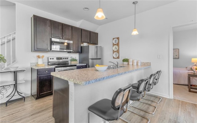 kitchen featuring hanging light fixtures, appliances with stainless steel finishes, light hardwood / wood-style floors, a kitchen bar, and kitchen peninsula