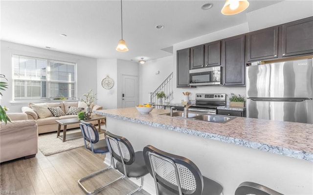 kitchen featuring appliances with stainless steel finishes, dark brown cabinetry, sink, light hardwood / wood-style flooring, and hanging light fixtures