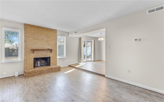 unfurnished living room featuring hardwood / wood-style floors, a textured ceiling, a wealth of natural light, and a brick fireplace