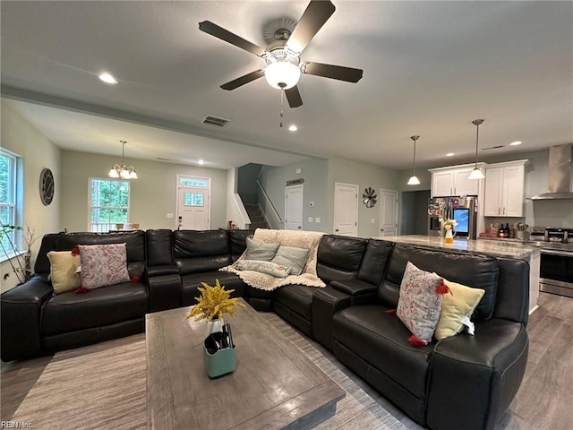 living room featuring ceiling fan with notable chandelier and light wood-type flooring