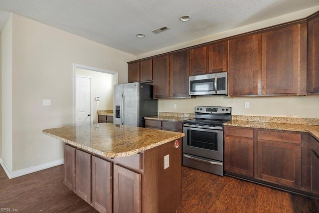 kitchen with a center island, dark wood-type flooring, appliances with stainless steel finishes, light stone counters, and dark brown cabinetry