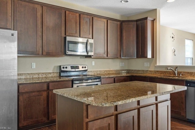 kitchen featuring light stone counters, dark brown cabinetry, stainless steel appliances, sink, and a kitchen island