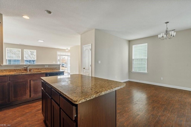 kitchen featuring sink, decorative light fixtures, a notable chandelier, a kitchen island, and light stone counters