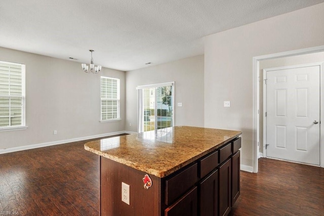 kitchen featuring pendant lighting, dark hardwood / wood-style floors, a notable chandelier, a kitchen island, and dark brown cabinetry