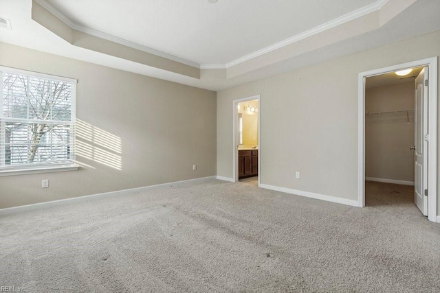 unfurnished bedroom featuring connected bathroom, a raised ceiling, crown molding, a walk in closet, and a closet