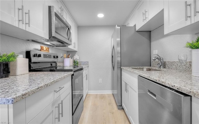 kitchen with appliances with stainless steel finishes, light hardwood / wood-style flooring, white cabinetry, and sink