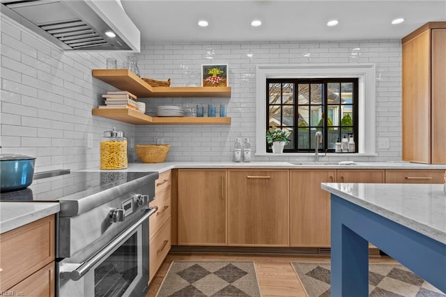 kitchen featuring light stone countertops, sink, wall chimney range hood, high end stove, and light wood-type flooring