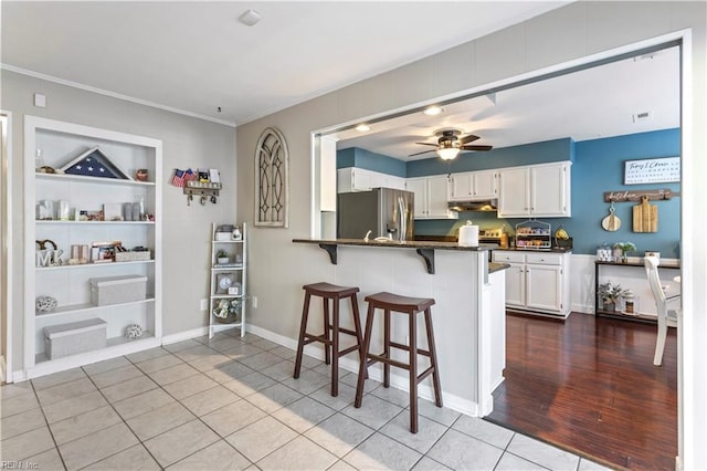 kitchen featuring kitchen peninsula, built in features, white cabinetry, stainless steel fridge with ice dispenser, and a breakfast bar area