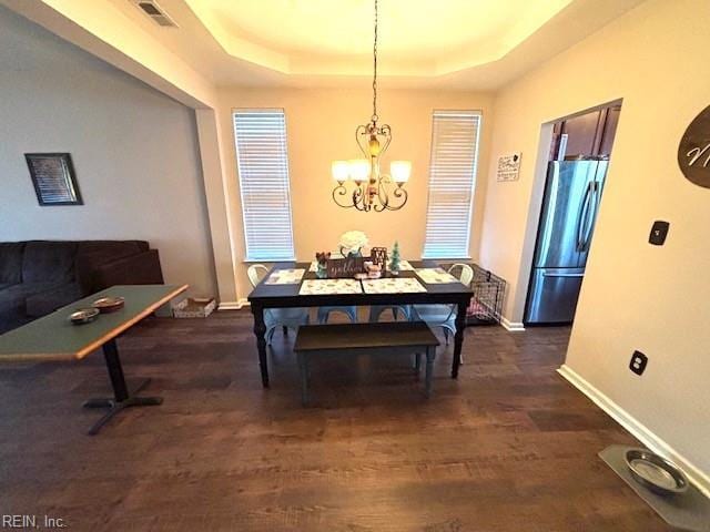 dining area featuring dark hardwood / wood-style flooring, a raised ceiling, and a notable chandelier