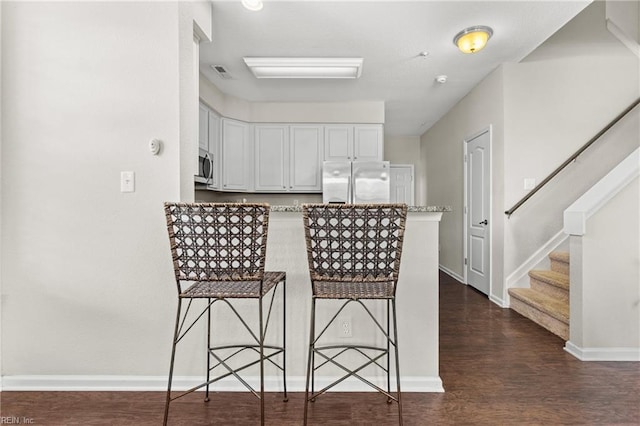 kitchen with a kitchen bar, appliances with stainless steel finishes, dark hardwood / wood-style flooring, light stone countertops, and white cabinetry