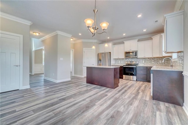 kitchen with a center island, sink, hanging light fixtures, stainless steel appliances, and ornamental molding