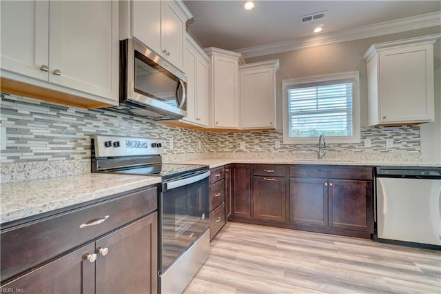 kitchen with decorative backsplash, stainless steel appliances, white cabinetry, and ornamental molding