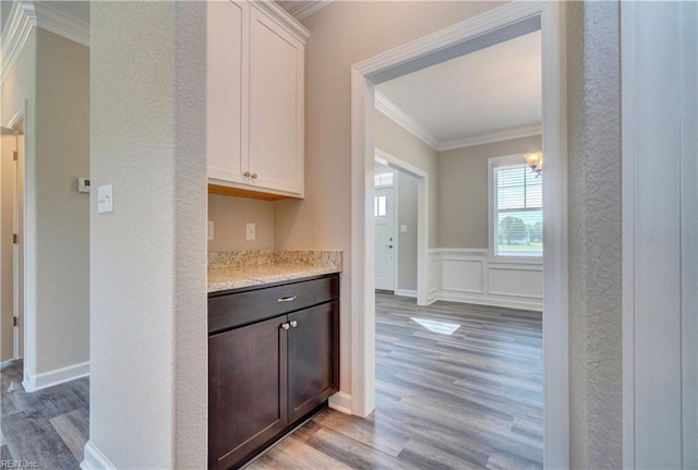 bar featuring dark brown cabinetry, crown molding, white cabinets, and light wood-type flooring