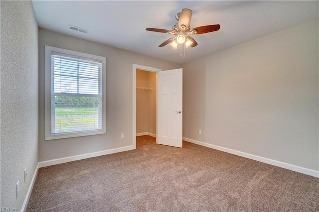 unfurnished bedroom with carpet flooring, ceiling fan, a spacious closet, and a closet