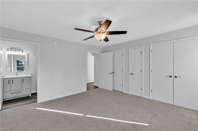 unfurnished bedroom with carpet, ceiling fan, sink, and two closets