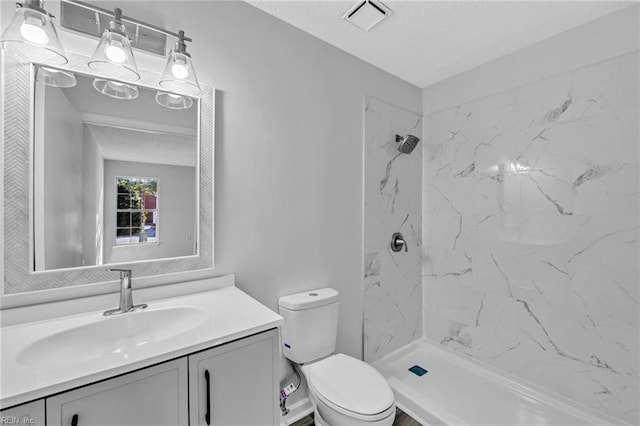 bathroom with vanity, toilet, a textured ceiling, and a tile shower