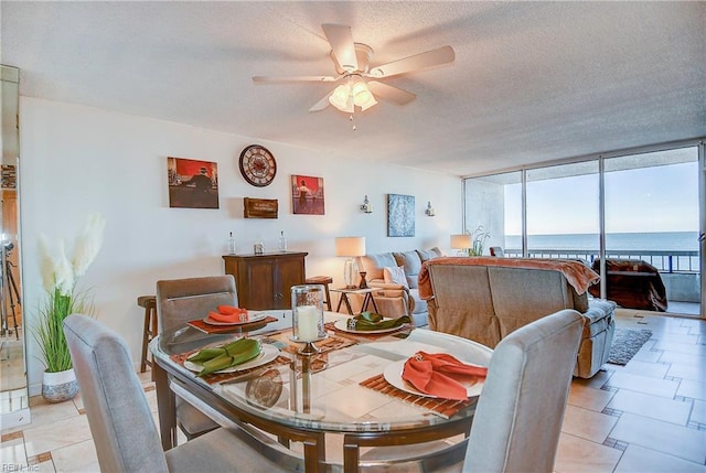 tiled dining space featuring ceiling fan, expansive windows, a water view, and a textured ceiling