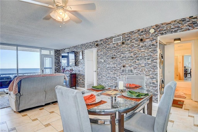 dining room with light tile patterned floors, a textured ceiling, stacked washer / dryer, and ceiling fan